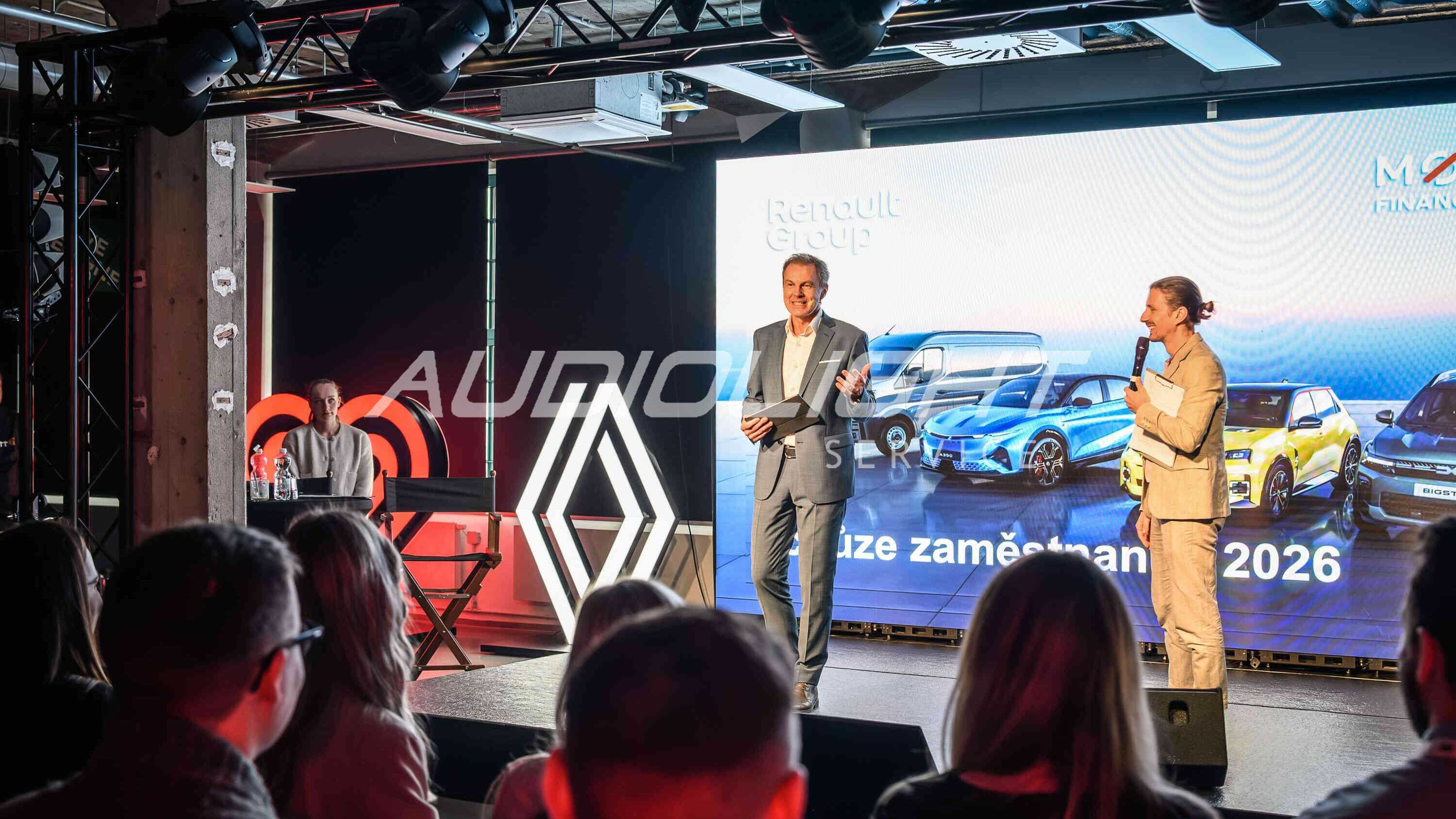 moderátor na podiu s logem společnosti